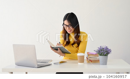 A female college student in glasses is making notes on her book while sitting at her desk. A female college student in glasses is making notes on her book while sitting at her desk. 104160957