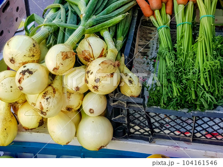 Close-up of fresh onions with a green feather and bunches of carrots on the counter of a vegetable store Close-up of fresh onions with a green feather and bunches of carrots on the counter of a vegetable store 104161546