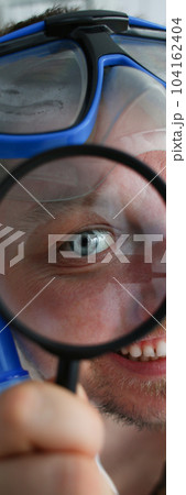 Portrait of a happy smiling manager in swimming goggles looks through magnifying glass Portrait of a happy smiling manager in swimming goggles looks through magnifying glass 104162404