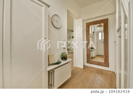 a hallway with wood flooring and a clock hanging on the wall above the door to the entranceway area a hallway with wood flooring and a clock hanging on the wall above the door to the entranceway area 104162419