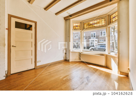 an empty living room with wood flooring and white brick walls in the background is a large window that looks out onto the street 104162628