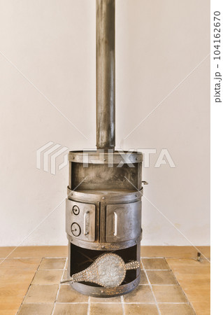 a wood burning stove in the corner of a room with tile floor and white wall behind it is an open door 104162670