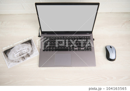 Top view panoramic X-ray photograph, radiographic scanner image of human teeth next to a laptop with blank digital screen on dentist's worktop. Diagnosis. Prevention. Teeth treatment. Dental practice 104163565