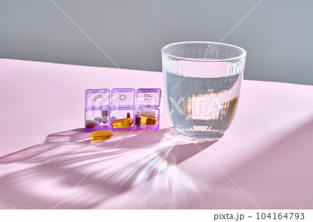Bright pill box with different pills and vitamins next to a glass of water. 104164793