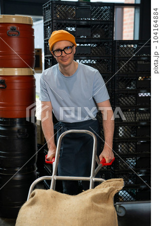 Roastery worker standing with sacks with coffee beans uploading. Roastery worker standing with sacks with coffee beans uploading. 104164884