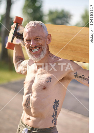 Smiling mature man holding longboard in a city park. 104165117