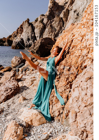Woman green dress sea. Woman in a long mint dress posing on a beach with rocks on sunny day. Girl on the nature on blue sky background. Woman green dress sea. Woman in a long mint dress posing on a beach with rocks on sunny day. Girl on the nature on blue sky background. 104167153