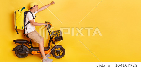 Shocked confident delivery man in cap riding bicycle with raised clenched fist, wearing thermo backpack bag isolated over yellow background. Mockup, advertisement area. Shocked confident delivery man in cap riding bicycle with raised clenched fist, wearing thermo backpack bag isolated over yellow background. Mockup, advertisement area. 104167728