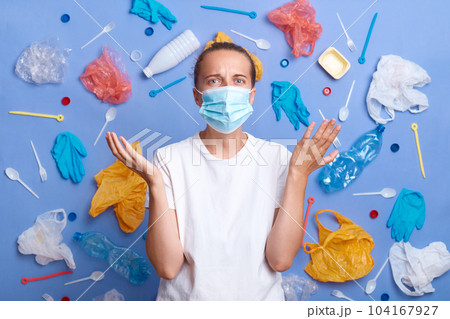 Shocked woman wears protective face mask, wearing white casual style T-shirt, looks unhappily, being disturbed by air pollution and serious problem of contamination, asking why. Shocked woman wears protective face mask, wearing white casual style T-shirt, looks unhappily, being disturbed by air pollution and serious problem of contamination, asking why. 104167927