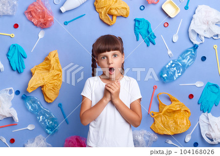 Shocked little girl with braids being shocked of air polution, saves Earth from contamination, astonished with harmful things destroying our planet, picked plastic litter isolated on blue wall. Shocked little girl with braids being shocked of air polution, saves Earth from contamination, astonished with harmful things destroying our planet, picked plastic litter isolated on blue wall. 104168026