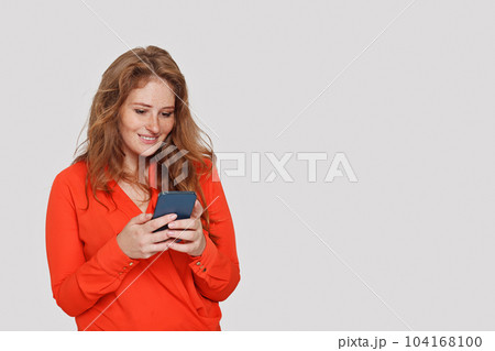 Attractive cheerful woman texting by phone on white studio wall background 104168100