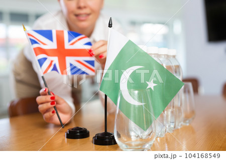 Little flag of Pakistan on table and flag of Great Britain put next to it by young woman 104168549