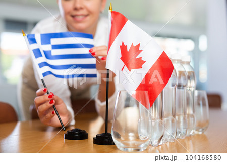 Young woman puts flags of Greece and Canada on table in office 104168580