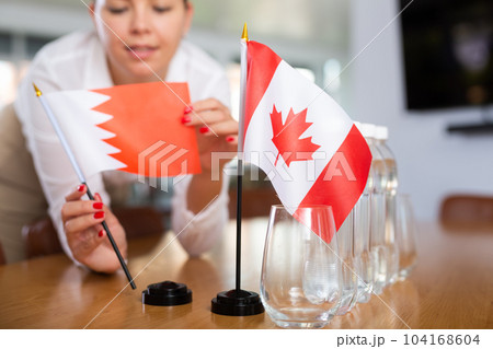 Little flag of Canada on table and flag of Bahrain put next to it by young woman Little flag of Canada on table and flag of Bahrain put next to it by young woman 104168604