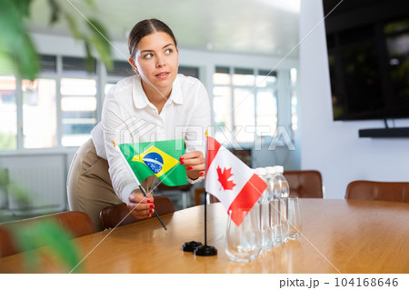 Positive young woman putting little flag of Brazil on table next to the flag of Canada Positive young woman putting little flag of Brazil on table next to the flag of Canada 104168646