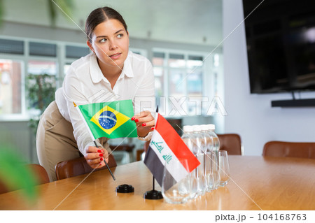 Young lady sets miniatures flags of Iraq and Brazil for international negotiations 104168763
