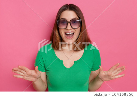 Indoor shot of excited astonished amazed woman wearing green t shirt posing isolated over green background, being positive surprised, standing with raised arms and open mouth. 104169550