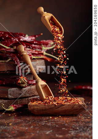 Chilli flakes are poured into a wooden dish. 104169650