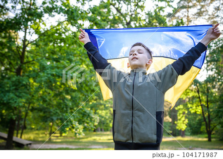 Pray for Ukraine. boy with Ukrainian flag running the summer park. Little kid waving national flag praying for peace. Happy child celebrating Independence Day Pray for Ukraine. boy with Ukrainian flag running the summer park. Little kid waving national flag praying for peace. Happy child celebrating Independence Day 104171987