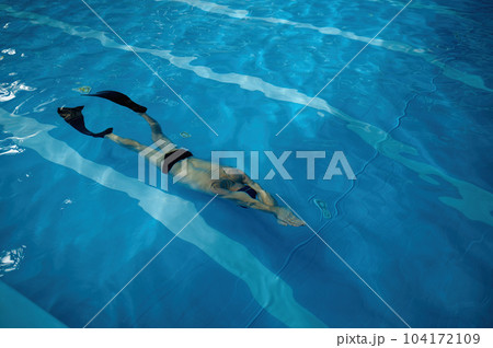 Senior man wearing goggles, cap and flippers swimming in indoor pool 104172109