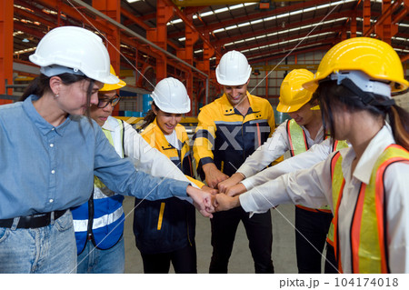 Group of male and female factory labor bumping fist together after finish meeting. Everyone wearing safety uniform and helmet. Workers working in the metal sheet factory. Group of male and female factory labor bumping fist together after finish meeting. Everyone wearing safety uniform and helmet. Workers working in the metal sheet factory. 104174018
