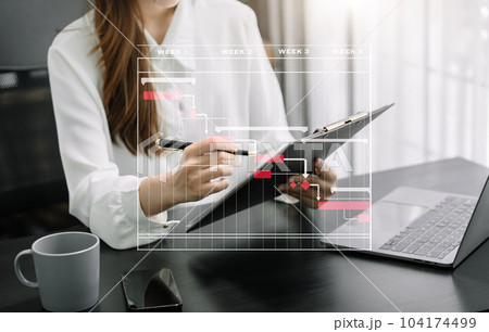 Business woman hand Project manager working and update tasks and Gantt chart scheduling virtual diagram.with smart phone, tablet and laptop in office. Business woman hand Project manager working and update tasks and Gantt chart scheduling virtual diagram.with smart phone, tablet and laptop in office. 104174499