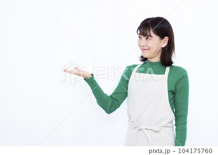 白い背景の前で紹介をしているエプロン姿の30代主婦 白い背景の前で紹介をしているエプロン姿の30代主婦 104175760