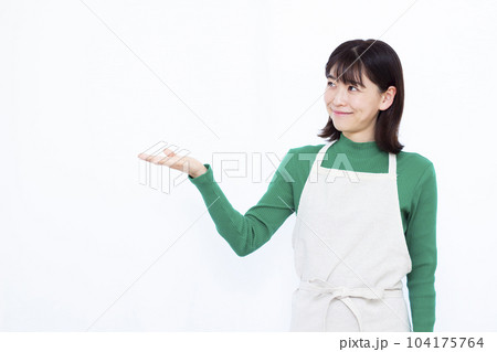白い背景の前で紹介をしているエプロン姿の30代主婦 白い背景の前で紹介をしているエプロン姿の30代主婦 104175764
