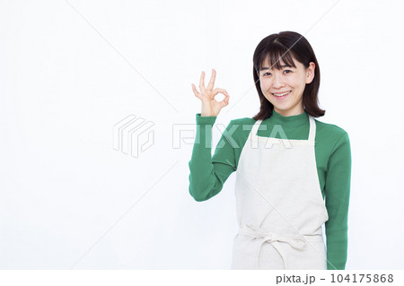 白い背景の前でOKサインをしているエプロン姿の30代主婦 104175868