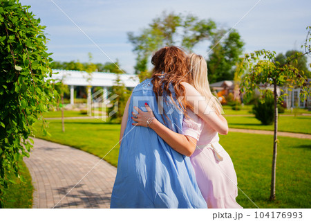rear view without faces. Two women in blue and pink dresses hugging in the park. rear view without faces. Two women in blue and pink dresses hugging in the park. 104176993
