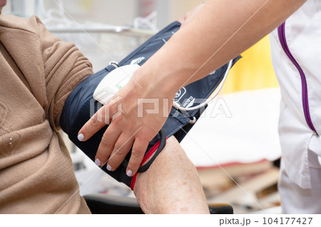Close up hand of nurse working and adjusting blood pressure gauge on senior woman hand in nursing 104177427