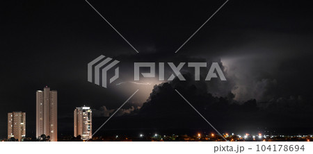 Three Skyscrapers Rise Above the Dark Cityscape During a Stormy Night Three Skyscrapers Rise Above the Dark Cityscape During a Stormy Night 104178694