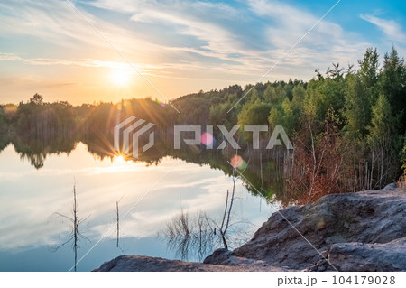 Beautiful landscape with colorful sunset over forest lake, Epic red and golden clouds above the 104179028