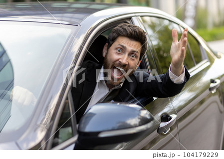 Joyful and happy car driver smiling and looking at camera, mature businessman waving his hand in greeting gesture, boss in business suit driving car. 104179229