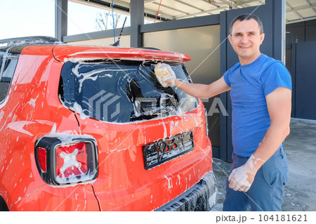 Young man washing his car with a sponge at a car wash. Manual car wash. Cleanliness concept Young man washing his car with a sponge at a car wash. Manual car wash. Cleanliness concept 104181621