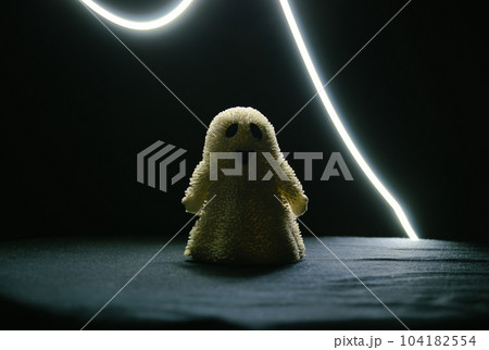A toy smiling ghost stands in the semi-darkness and a strip of light above it A toy smiling ghost stands in the semi-darkness and a strip of light above it 104182554