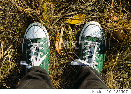 Men feet in green and white sneakers with white laces stand on the autumn grass Men feet in green and white sneakers with white laces stand on the autumn grass 104182567