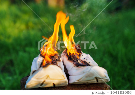 Burning leather sports shoes. Sneakers or gym shoes on fire stand on the Stump. Burning leather sports shoes. Sneakers or gym shoes on fire stand on the Stump. 104183006