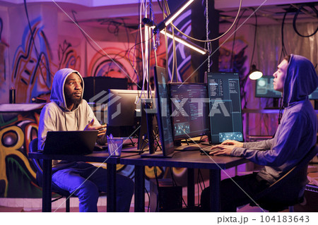 Internet criminals planning cyberattack and malicious software programming. Asian and african american hackers talking about illegal ransomware coding while cracking password on computers Internet criminals planning cyberattack and malicious software programming. Asian and african american hackers talking about illegal ransomware coding while cracking password on computers 104183643