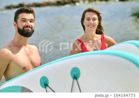 Attractive man and woman young surfers on beach, enjoying vacation near sea and extreme sport. Attractive man and woman young surfers on beach, enjoying vacation near sea and extreme sport. 104184773