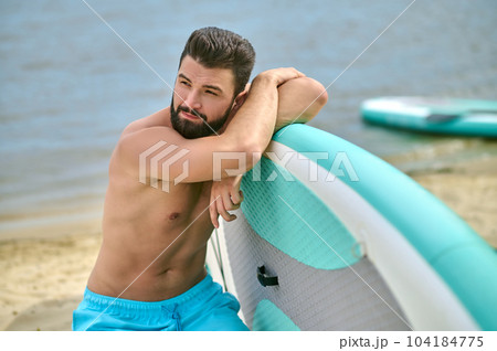 Man standing with paddle board on sandy beach near ocean , sup water sport, active summer activity. Man standing with paddle board on sandy beach near ocean , sup water sport, active summer activity. 104184775