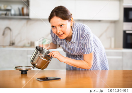 Inexperienced housewife holds saucepan in hands and calls asking for cooking advice 104186495