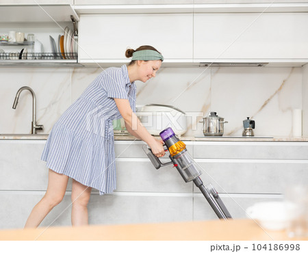 Housewife using vacuum cleaner removes dust in room Housewife using vacuum cleaner removes dust in room 104186998