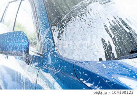 Blue car wash with white soap foam. Auto care business. Car cleaning service. Vehicle cleaning service. Foam wash car detailing. The windshield of blue luxury SUV car is covered with white foam. 104190122