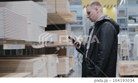A man in a hardware store chooses wooden sheets of osb. The buyer in the store chooses chipboard. Buying plywood at a hardware store. Blockboards in a hardware store A man in a hardware store chooses wooden sheets of osb. The buyer in the store chooses chipboard. Buying plywood at a hardware store. Blockboards in a hardware store 104193034