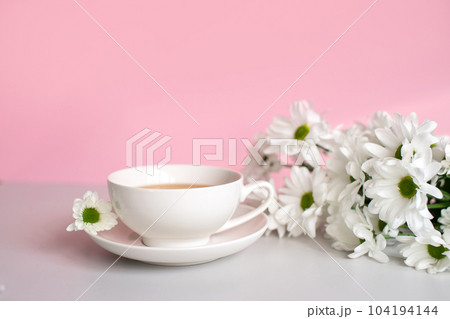 White set cup with plate stand on a pink background with white chamomile flowers 104194144