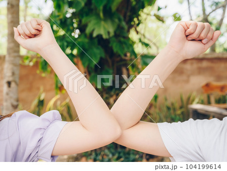 Cropped shot of two women bump elbows for greeting during coronavirus epidemic. Cropped shot of two women bump elbows for greeting during coronavirus epidemic. 104199614