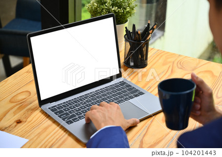 Closeup shot businessman drinking hot coffee and using laptop on wooden office desk 104201443