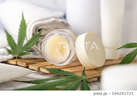 Jar with CBD lip balm near green cannabis leaves near bottles and towel close up Jar with CBD lip balm near green cannabis leaves near bottles and towel close up 104201725