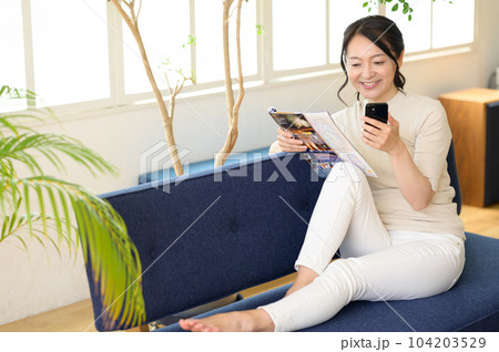 スマホを片手にパンフレットを見るミドル女性 104203529